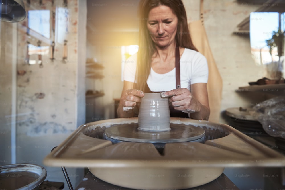 Artigiana che usa le mani per modellare un pezzo di argilla bagnato che gira su un tornio mentre è seduta nel suo laboratorio di ceramica