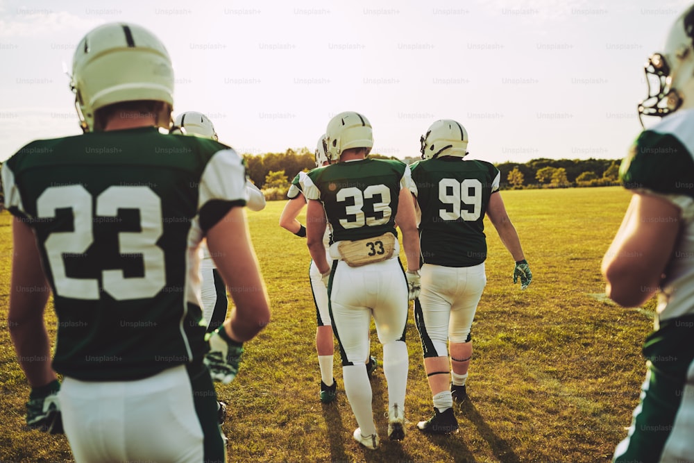 Group of young American football players walking together outside on a grassy field in the afternoon during a practice session