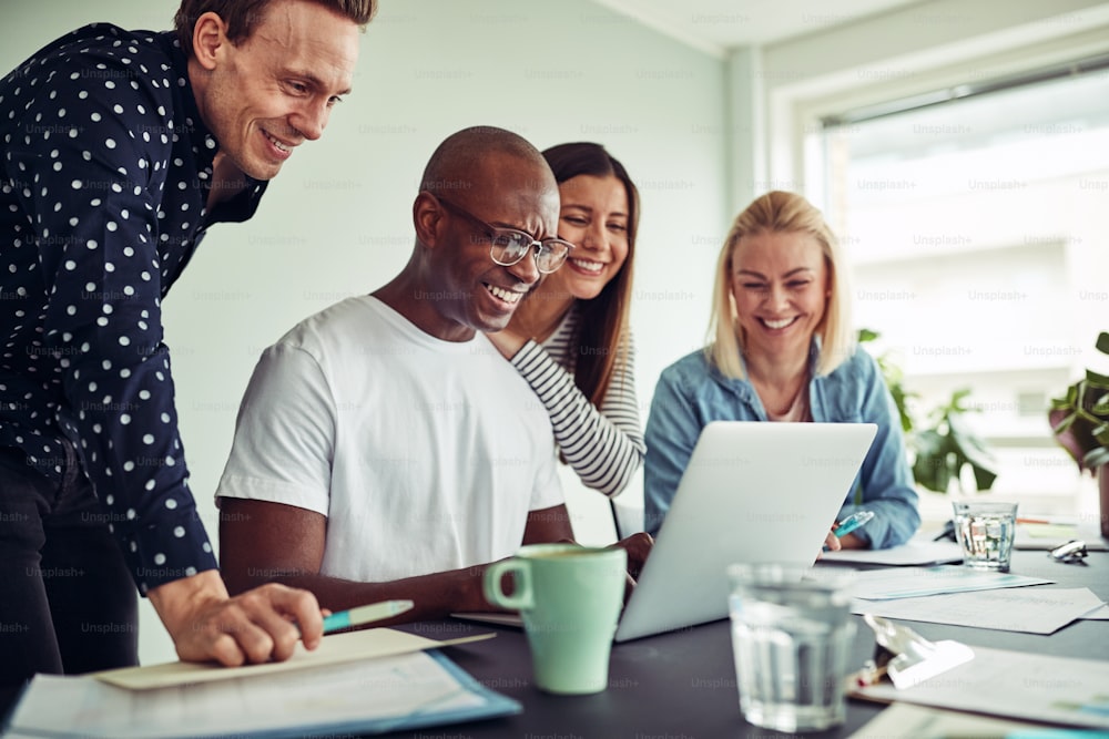 Diverse group of smiling businesspeople working together over a laptop at a table in a modern office