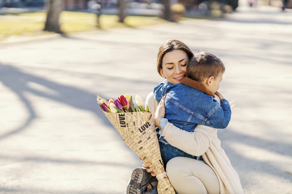 A little boy embracing mom with flowers on mother's day.