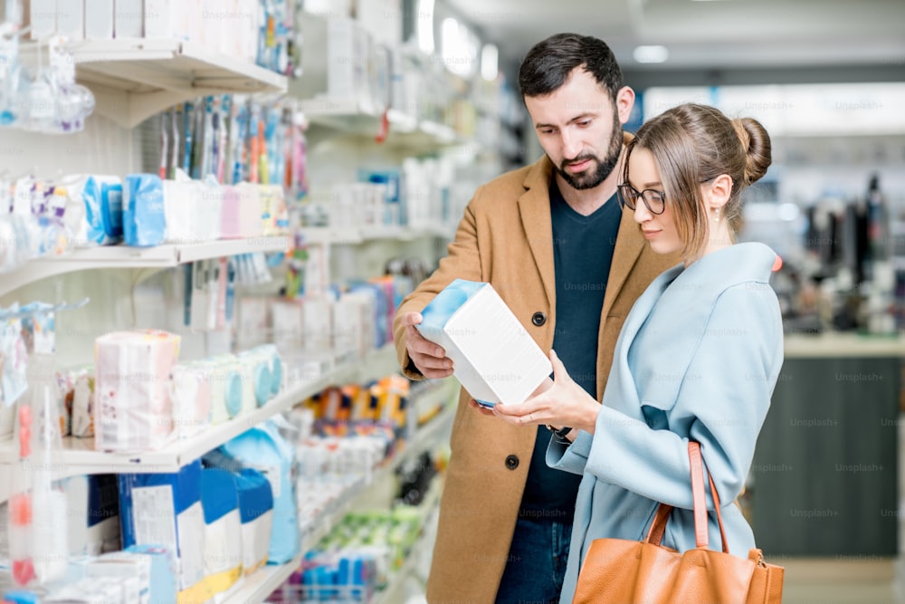 Young couple dressed in coats choosing medicine standing with box in the pharmacy store