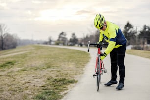 An old bicyclist checking on front tire on a bicycle.