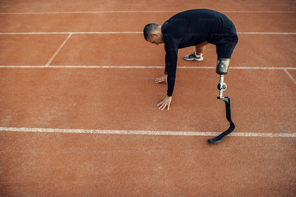 Um esportista em forma com perna artificial se exercitando no estádio em pista de corrida.