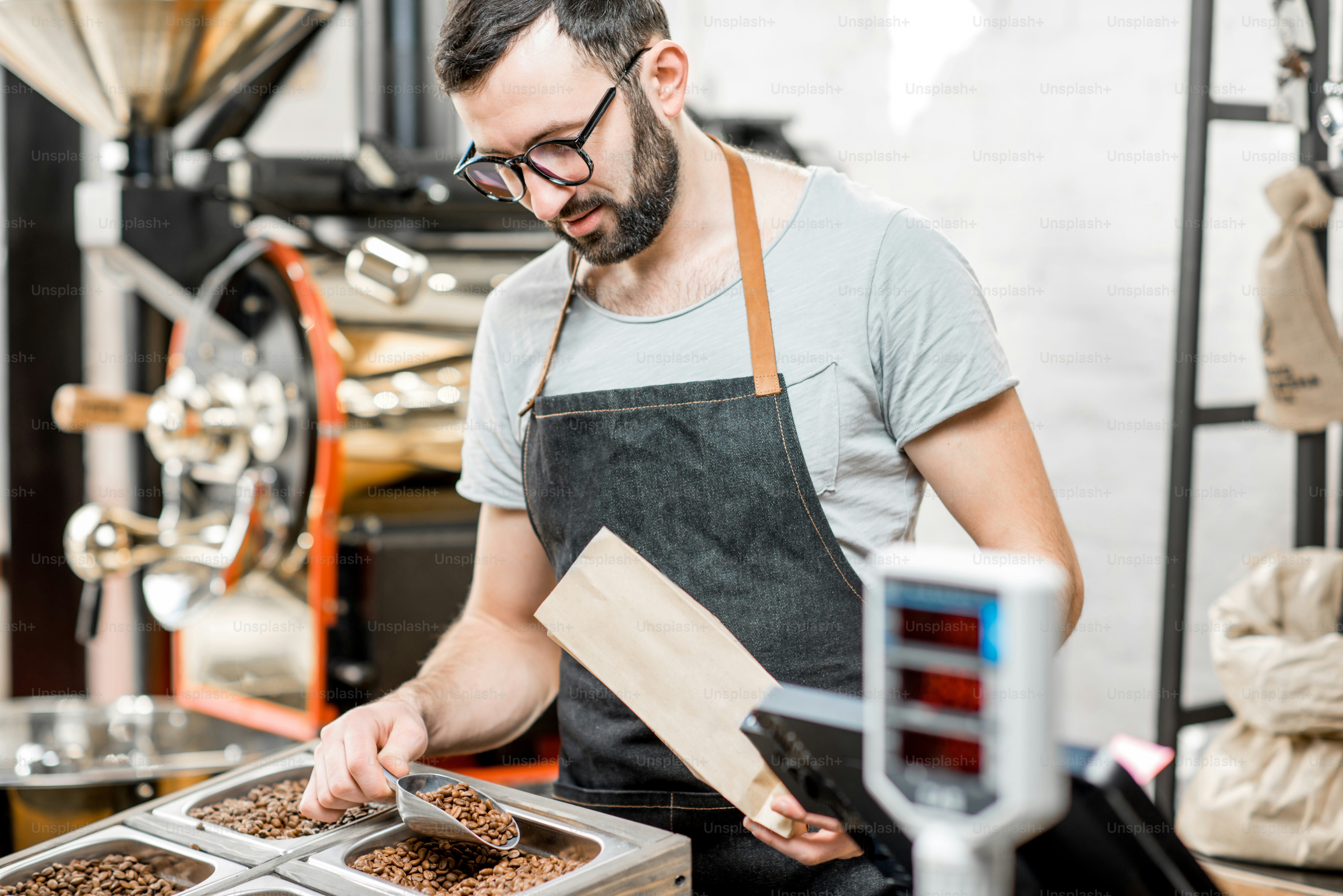 Male seller in uniform filling bag with coffee beans working in the coffee store
