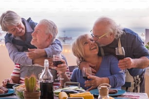 Dos parejas maduras se quedan juntas con sonrisas de amor y besos durante una cena al aire libre en la terraza de la azotea con vista al mar y a los tejados. alegría y diversión en la actividad de ocio por la noche y el concepto de amistad para siempre