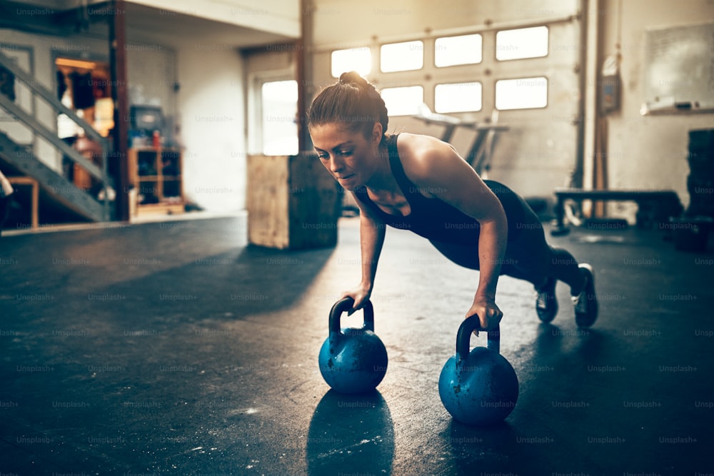 Fit young woman doing pushups on dumbbells while working out alone in a gym