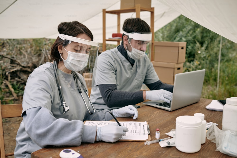 Two young volunteers filling in medical documents and entering data in database while working in refugee camp