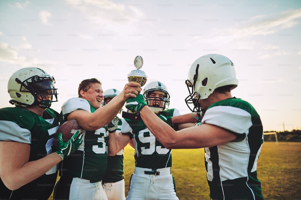 Ecstatic group of American football players standing in a huddle on a field raising a championship trophy in celebration