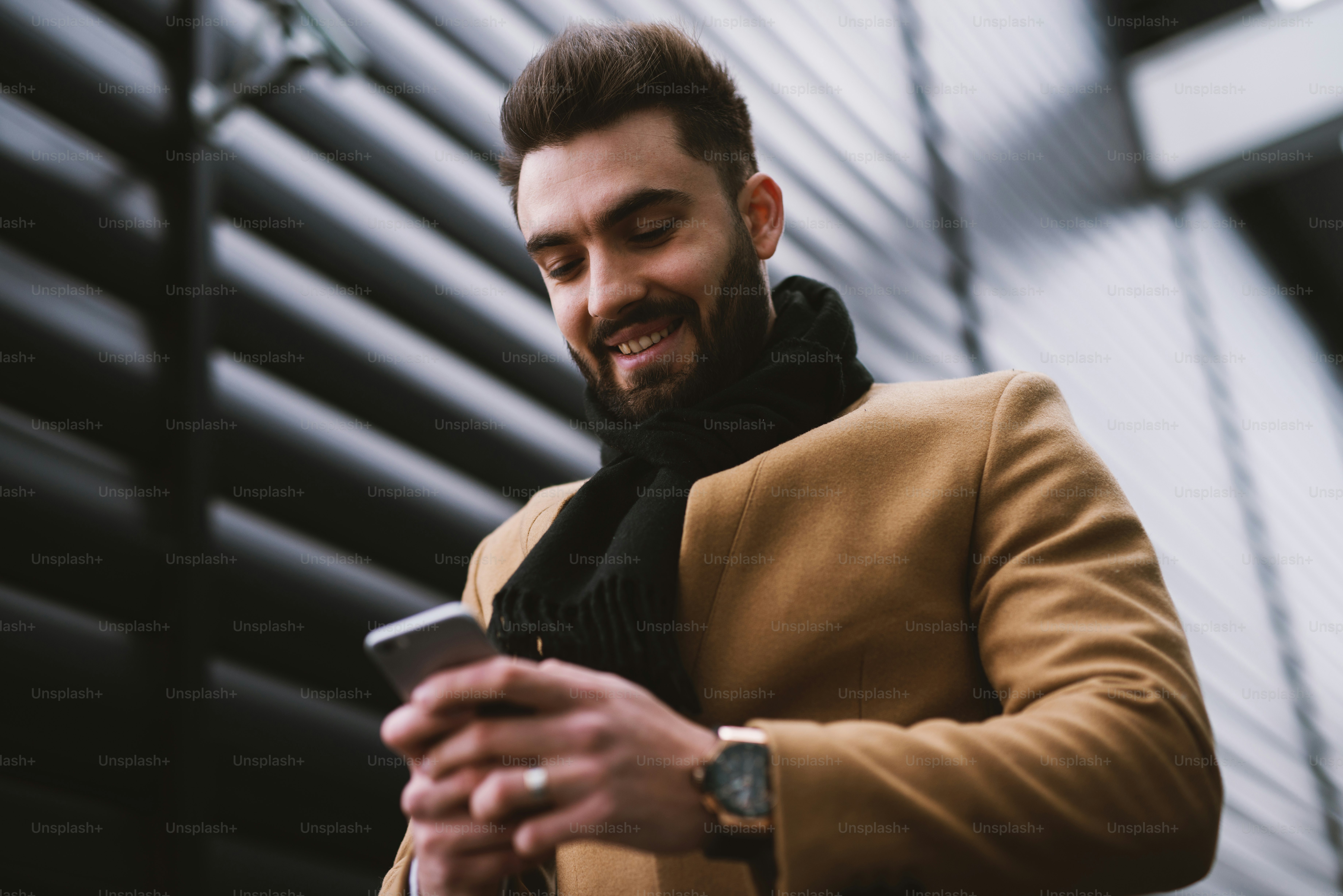 通りを歩いているときに電話を見ながら微笑むハンサムな若い男。