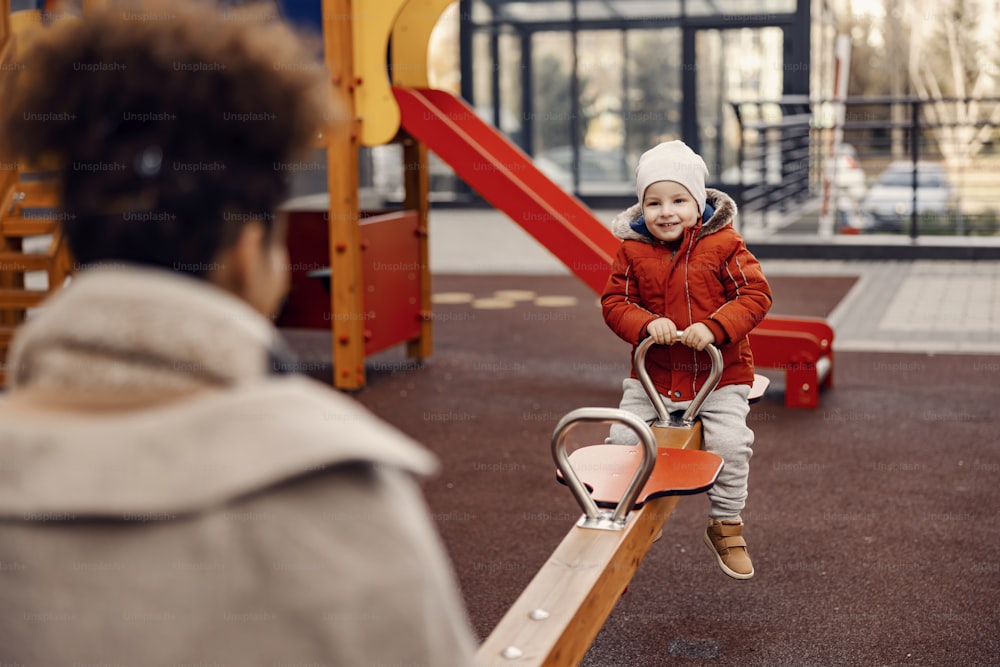 Mère et fils s’amusent sur une balançoire sur l’aire de jeux. Heureux petit garçon mignon assis sur une balançoire avec sa mère et s’amusant.