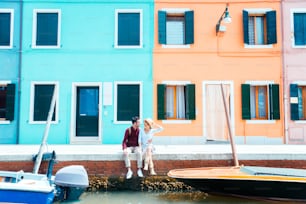 Giovane coppia che visita in vacanza Venezia, Italia - due turisti che si siedono sul canale veneziano durante l'estate - Persone, vacanze e concetto di stile di vita.