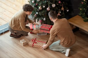 Parents putting Christmas gifts under decorated tree while preparing it for kids