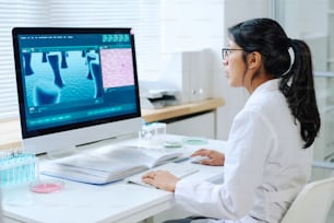 Giovane virologa ispanica con capelli lunghi scuri che studiano il nuovo virus mentre si siedono sulla scrivania davanti al computer in laboratorio