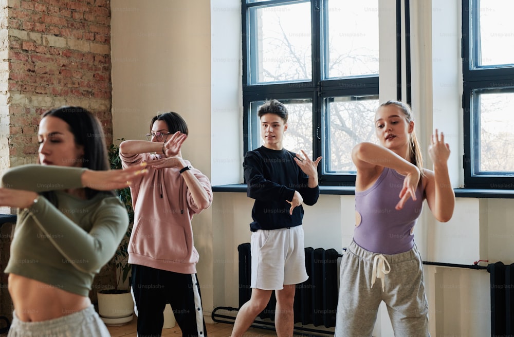 Giovane istruttore maschio del gruppo di ballo alla moda che consulta ragazze adolescenti e ragazzo in abbigliamento sportivo che ripete il nuovo movimento durante l'allenamento