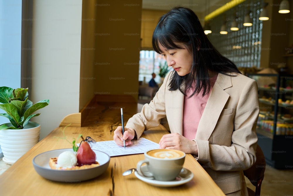 Young candidate filling application for job while sitting at table with dessert and coffee in coffee shop