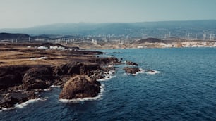 Vista aérea da costa de rochas e ondas do oceano com pequena cidade ao fundo. Céu azul e ondas do oceano com moinhos de vento e montanhas. Conceito de viagem e lugar cênico