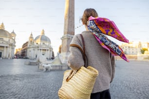 La donna cammina su Piazza del Popolo nella città di Roma in un momento mattutino. Persona femminile con borsa e scialle colorato tra i capelli. Concetto di stile di vita e di viaggio italiano