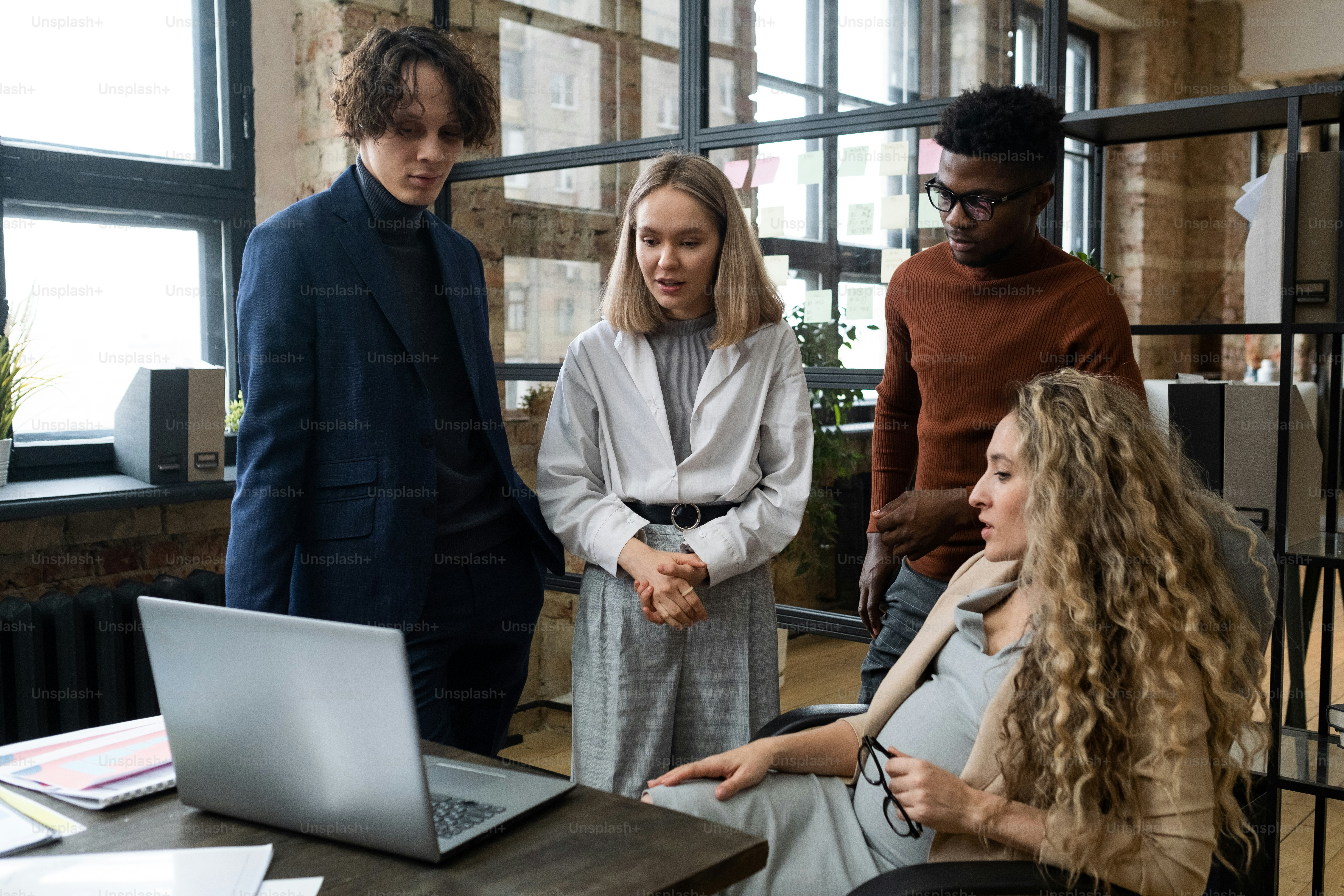 Pregnant businesswoman discussing online presentation on laptop with her employees during their teamwork at office