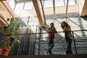 Giovani appuntamenti interrazziali in abbigliamento casual alla moda in piedi sul balcone in un loft o in un monolocale con pareti di mattoni grigi e chiacchierare