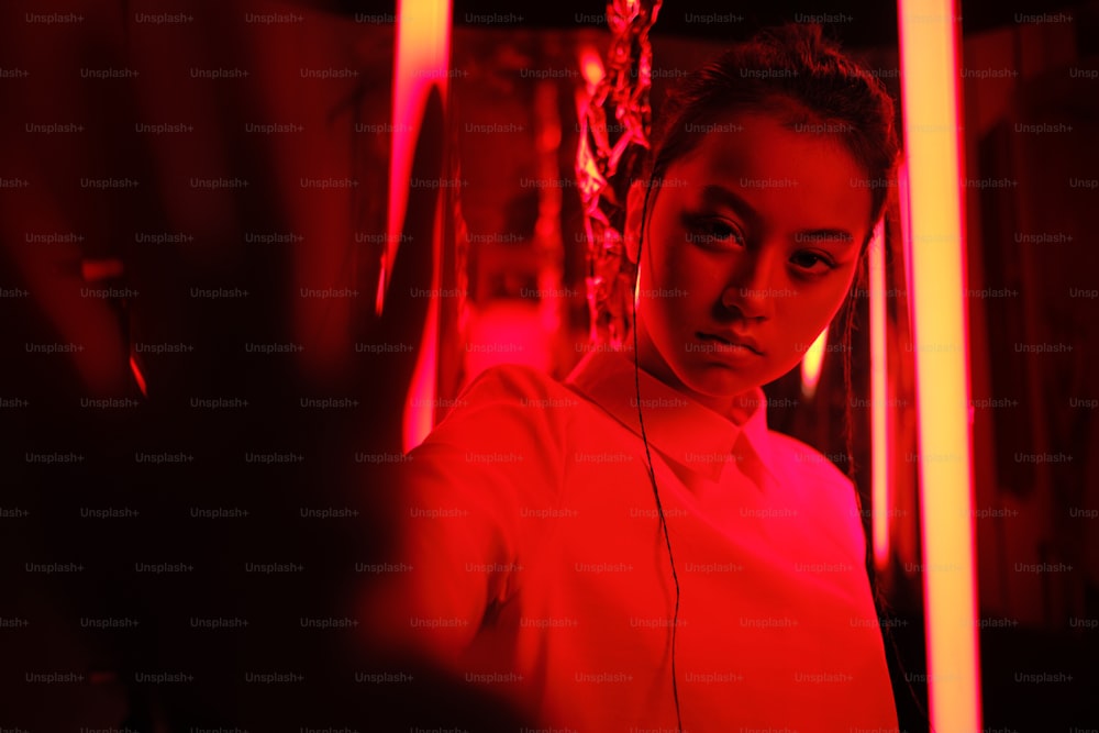 赤いネオンライトの中で、カメラに向かって手を持つ若いアジアの10代の女の子の肖像画。サイバーで未来的なポートレートのコンセプト