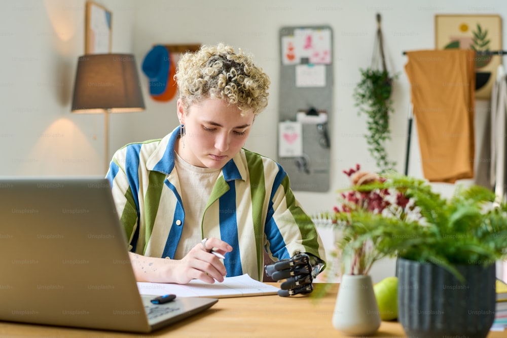 Joven empresaria moderna o empleada con brazo parcial mirando documentos financieros mientras trabaja en la oficina en casa