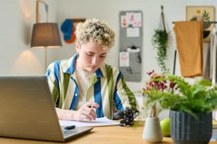 Young modern businesswoman or female employee with partial arm looking through financial documents while working in home office