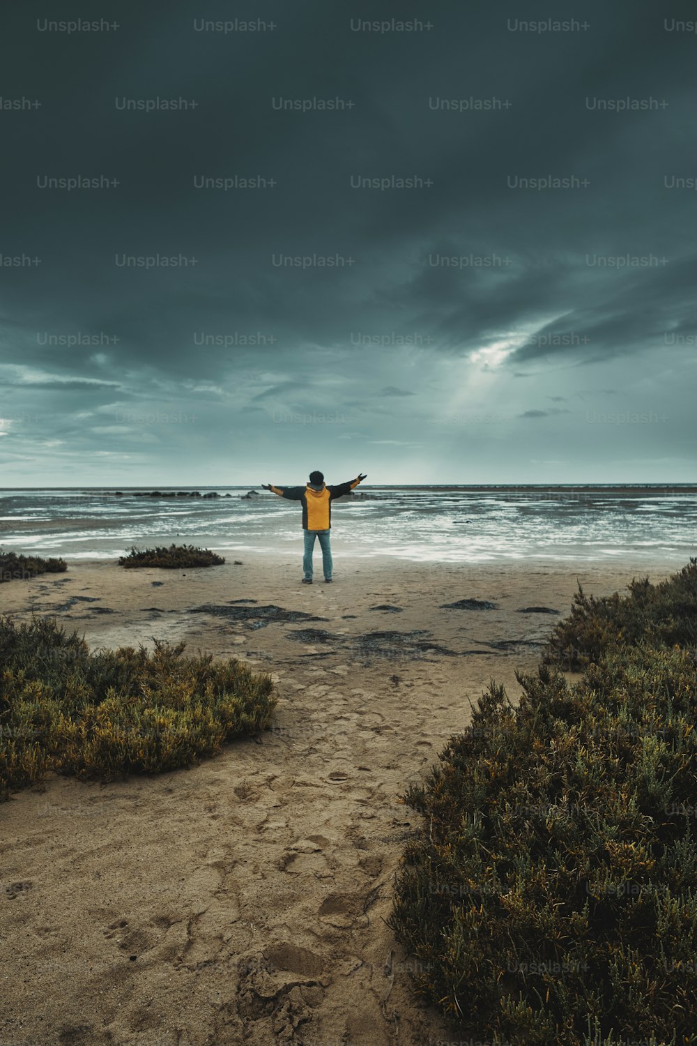 Concept of climate change for global warming people. Man standing against bad weather with black and blue clouds and flood water ground. Adventure people at the beach and epic landscape