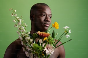 Homem sereno jovem da etnia africana com buquê de flores bonitas frescas sobre o fundo verde