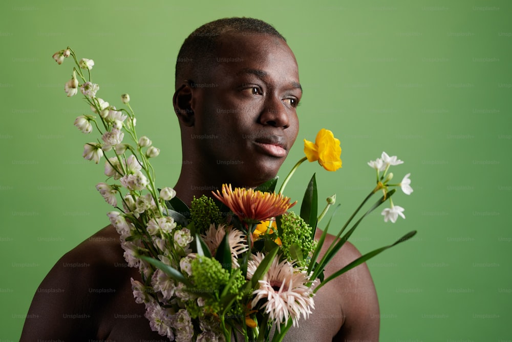 Young serene man of African ethnicity with bouquet of fresh beautiful flowers over green background