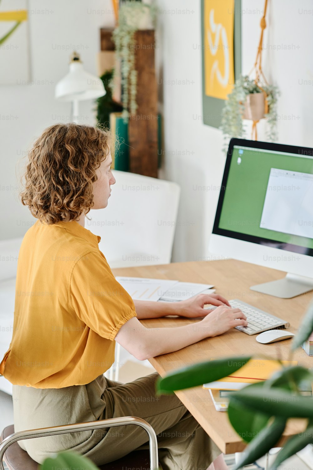 Jovem webdesigner freelancer em trajes casuais com as mãos sobre o teclado olhando para o documento eletrônico na tela do computador