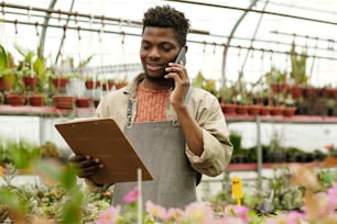 Propriétaire d’un magasin de fleurs regardant un document dans ses mains et prenant une commande d’un client par téléphone portable