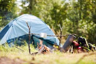 Tourists cooking something to eat in small pan hanging on branch over bonfire in the forest