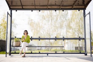 Woman with flowerpot at modern bus stop outdoors, wide front view with copy space. Concept of public transportation and sustainability