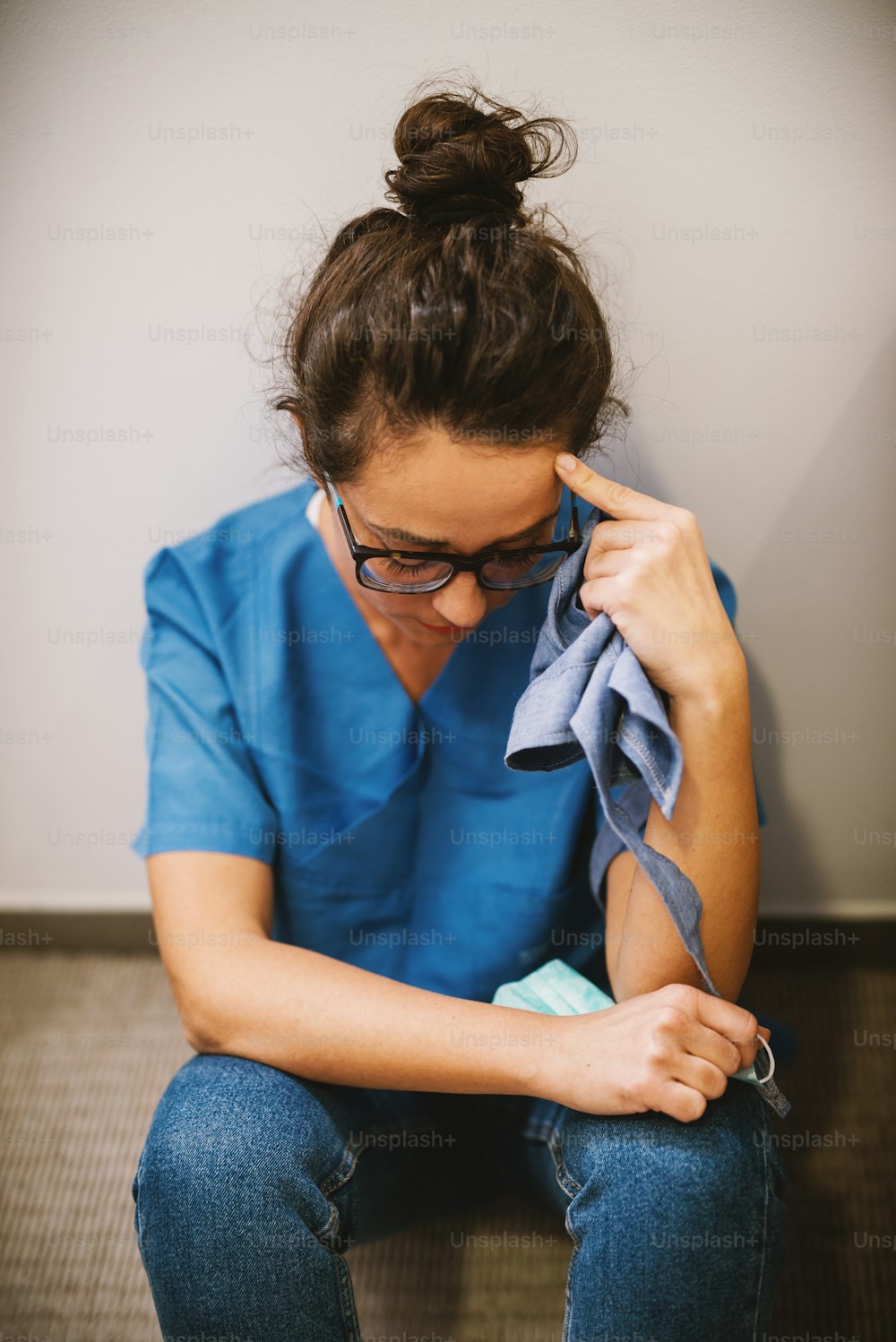 Portrait of middle age woman surgeon sitting on the floor leaned on the wall after an operation and praying by looking down.