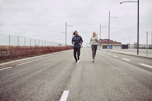 Casal jovem diversificado em roupas esportivas olhando focado enquanto correm juntos ao longo de uma estrada no país
