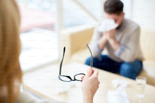 Anonymous woman holding eyeglasses while having depressed patient at reception