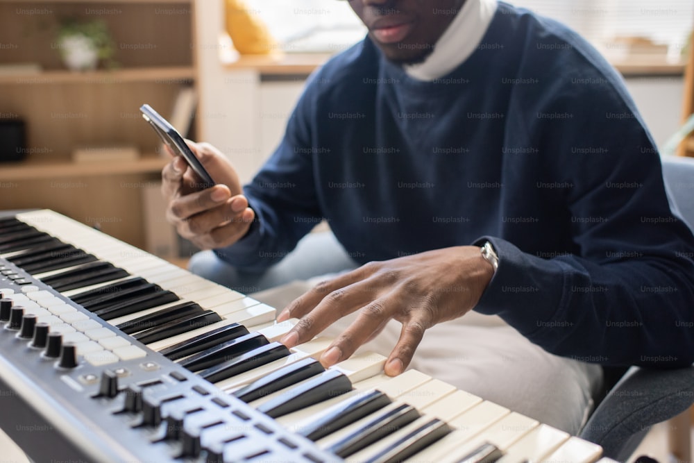 Young male teacher of music with smartphone touching keys of piano keyboard during lesson in studio