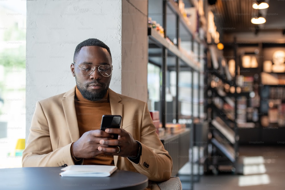 Serious man of African ethnicity scrolling in mobile phone while resting in bookshop