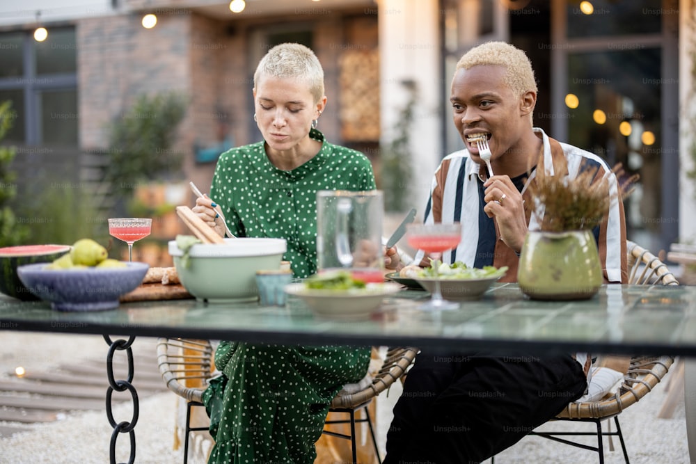 Multiracial couple talking and having fun during a dinnertime at their garden of country house. Idea of a warm conversation and relationship. Latin man and european woman enjoying time together