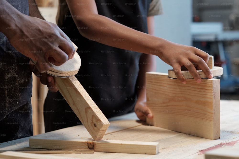 アフリカ系アメリカ人の父と息子がワークショップで一緒に木製家具を建てるクローズアップ、コピースペース