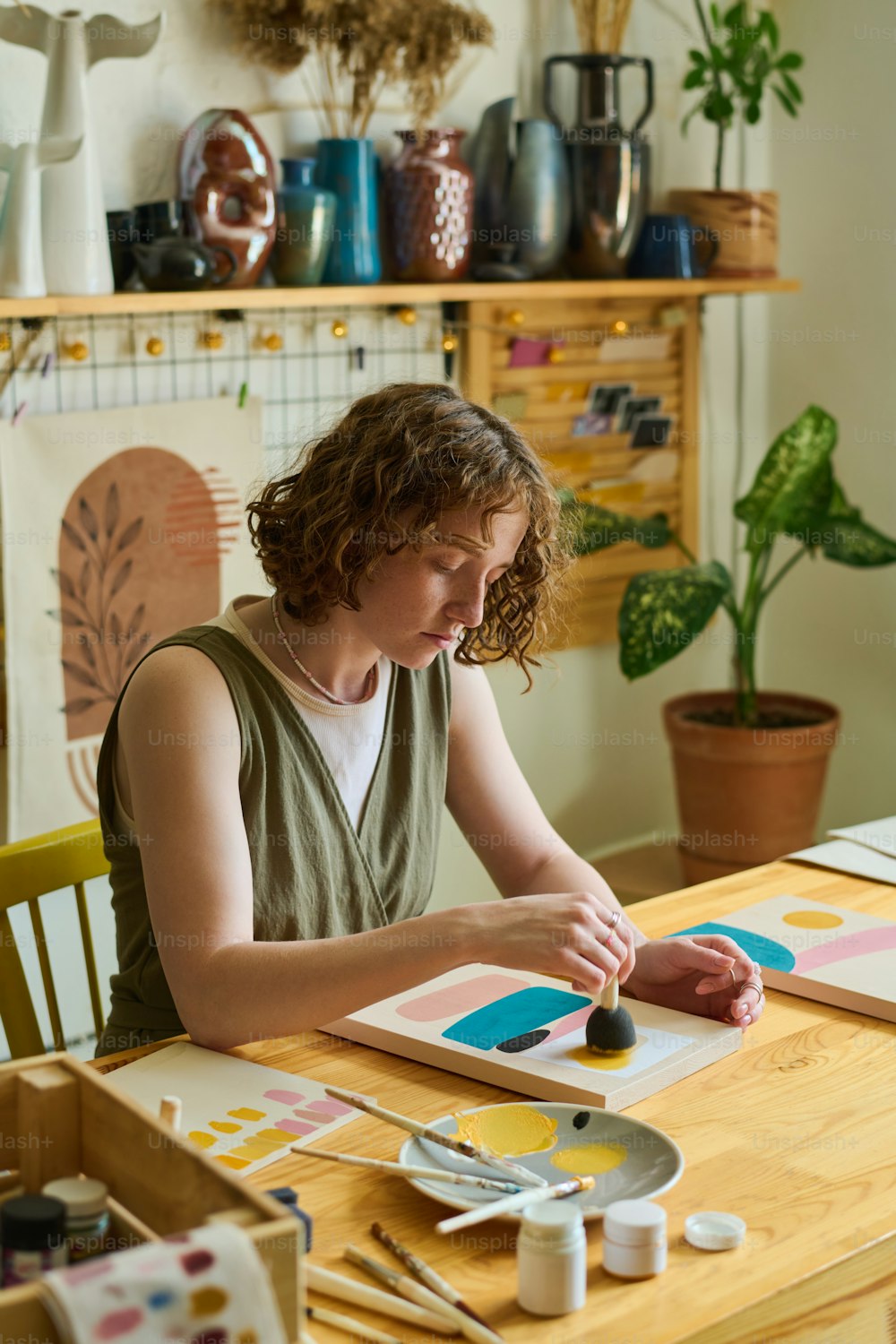 Artista feminina criativa em casualwear usando esponja para aplicar cor no papel enquanto trabalha sobre a nova pintura abstrata na oficina