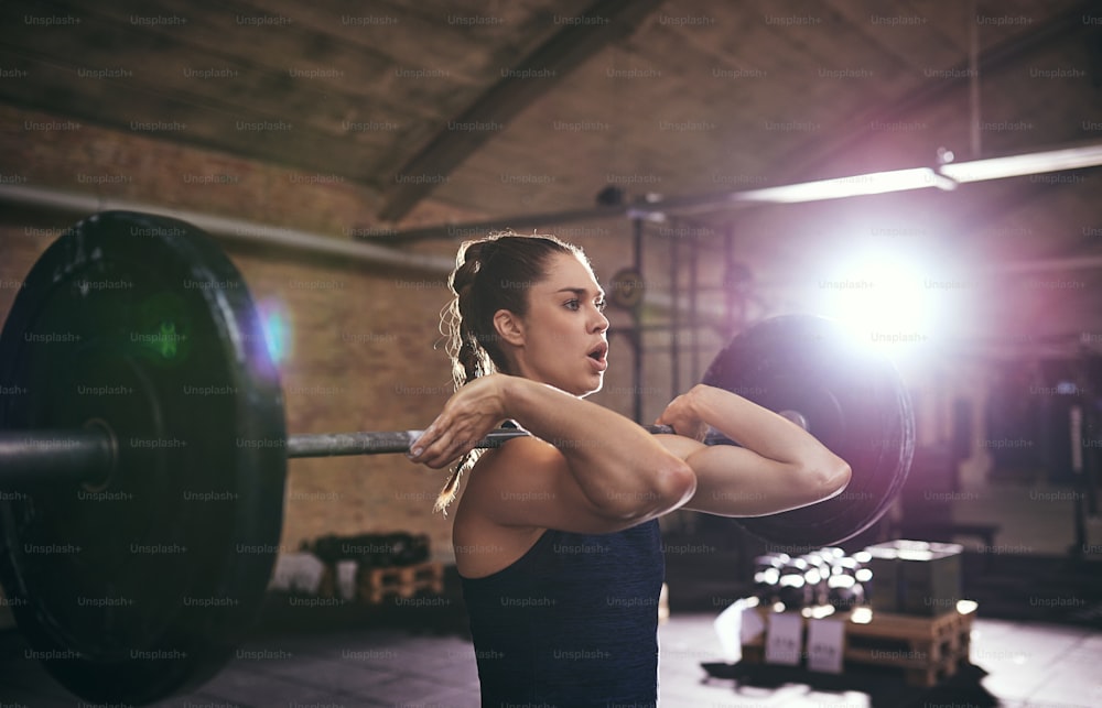Young woman with mouth opened exercising with barbell. Horizontal indoors shot