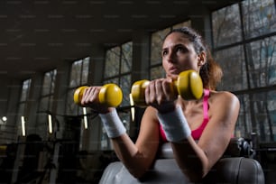 Strong young woman with yellow dumbbells making exercises in gym
