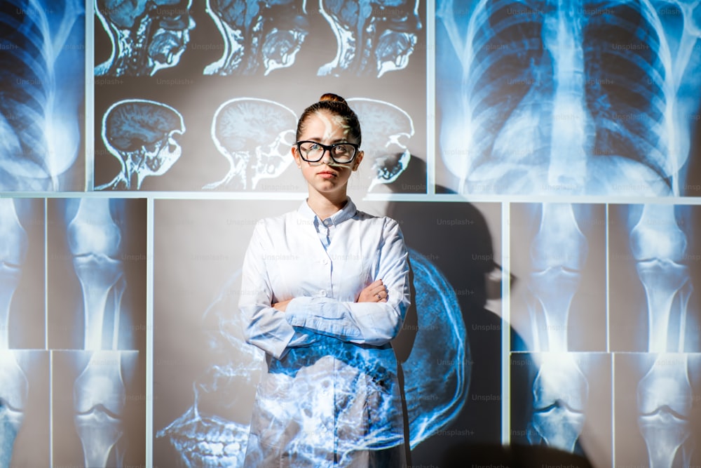 Ritratto di una giovane donna medico in uniforme con radiografie proiettate di parti umane