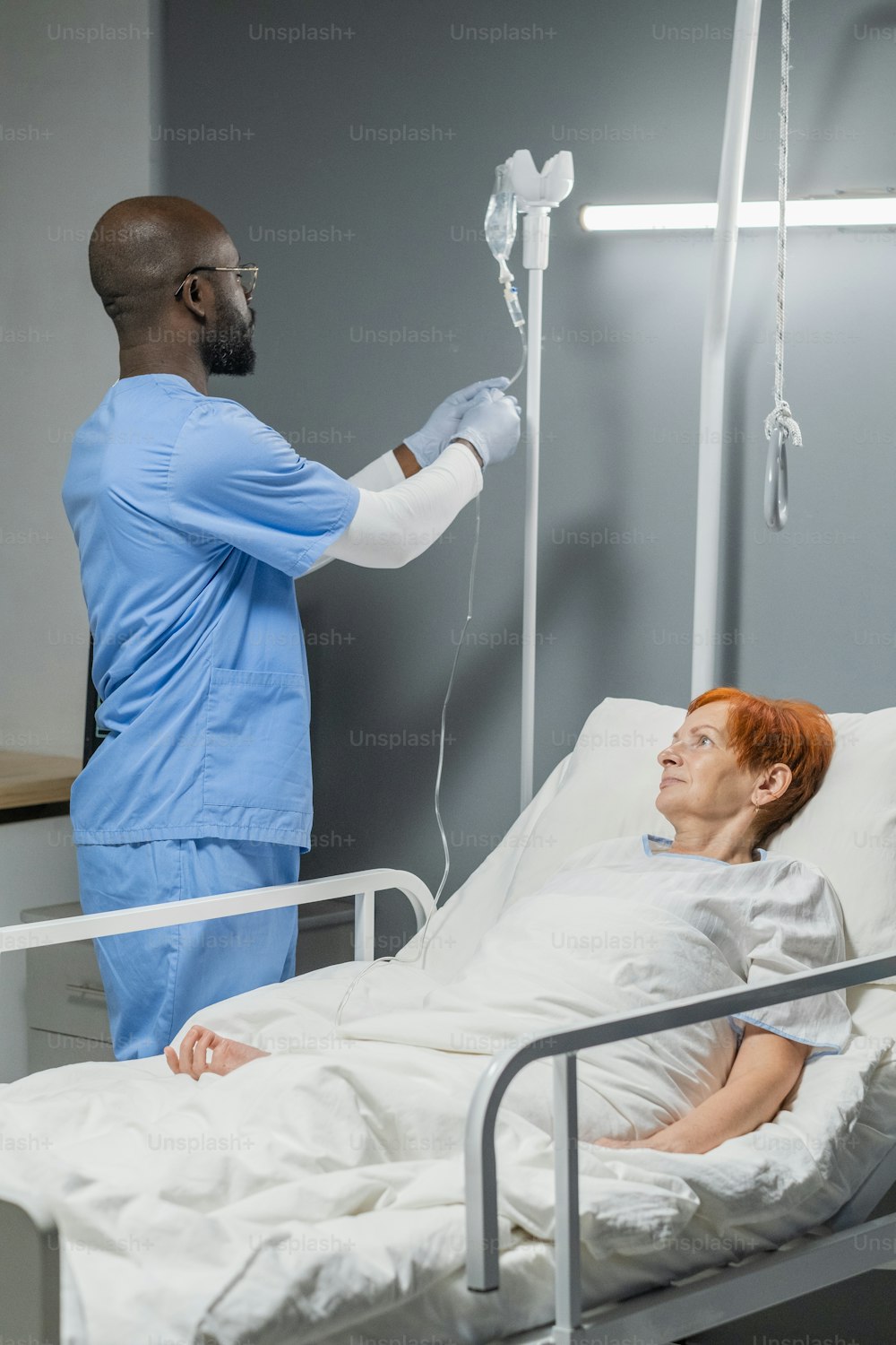 制服を着たアフリカの麻酔科医は、病院のベッドに横たわっている間、病気の高齢女性のためにスポイトを作ります