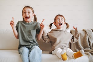 Divertente felice due bambini ragazze sorelle che si divertono sul divano a casa