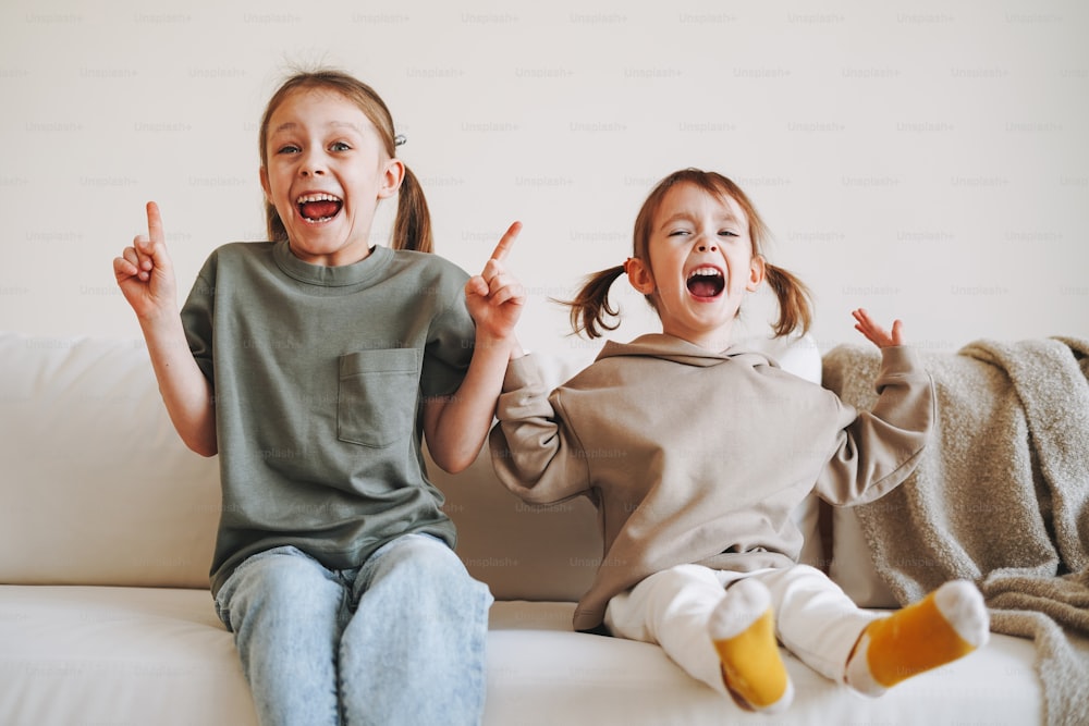Dos niñas felices divertidas hermanas divirtiéndose en el sofá de casa