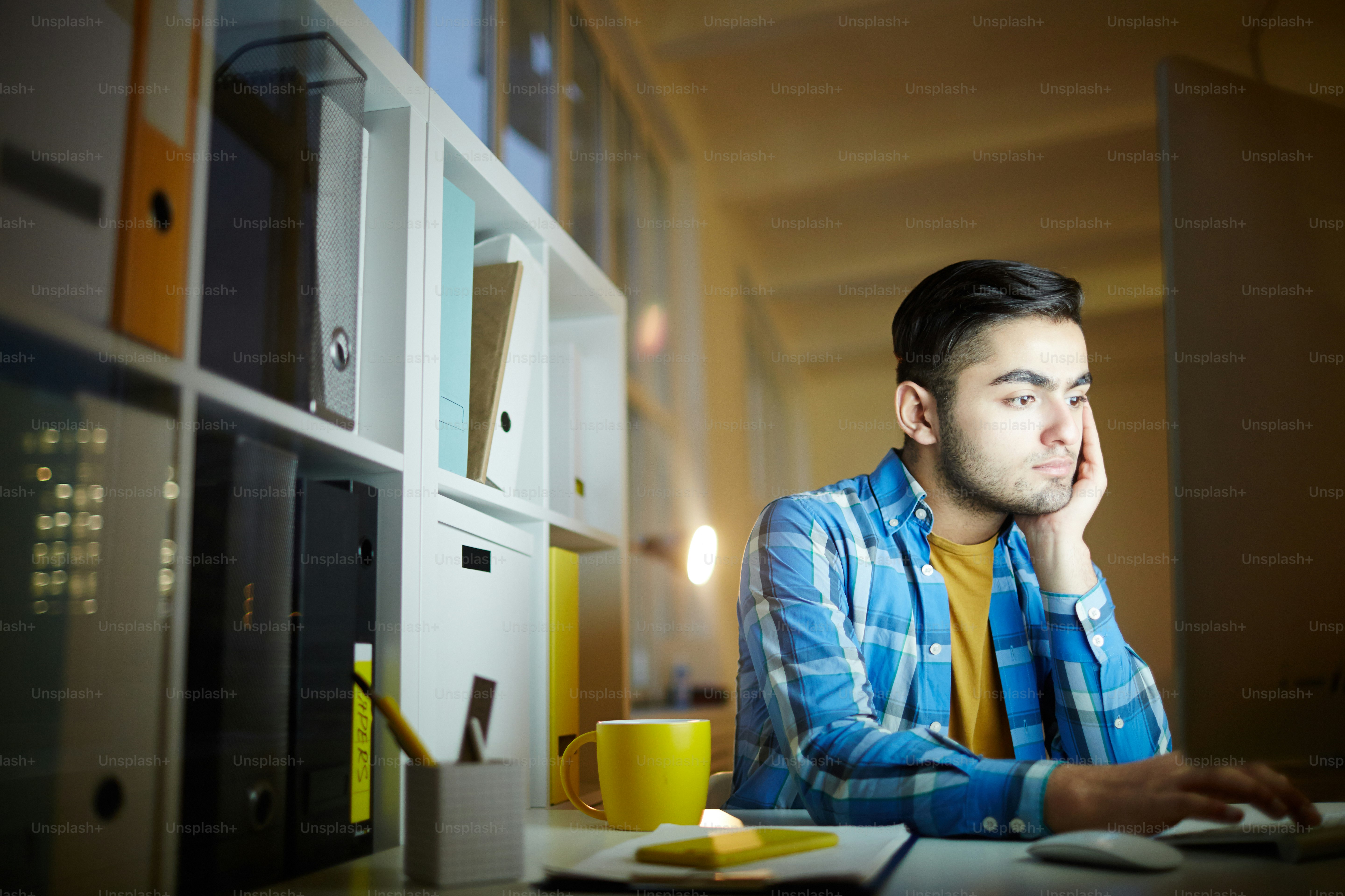 Junge Mitarbeiterin in Freizeitkleidung sitzt abends im Büro vor dem Monitor