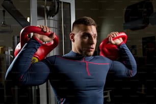 Strong muscular athlete lifting heavy kettlebars during physical training