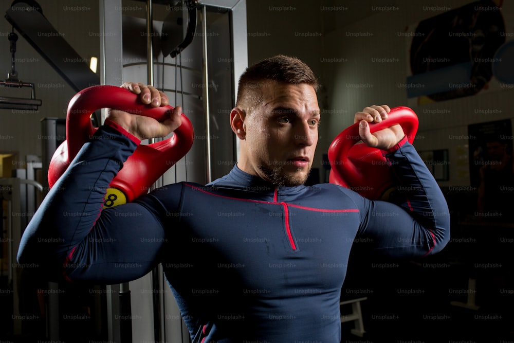 Strong muscular athlete lifting heavy kettlebars during physical training